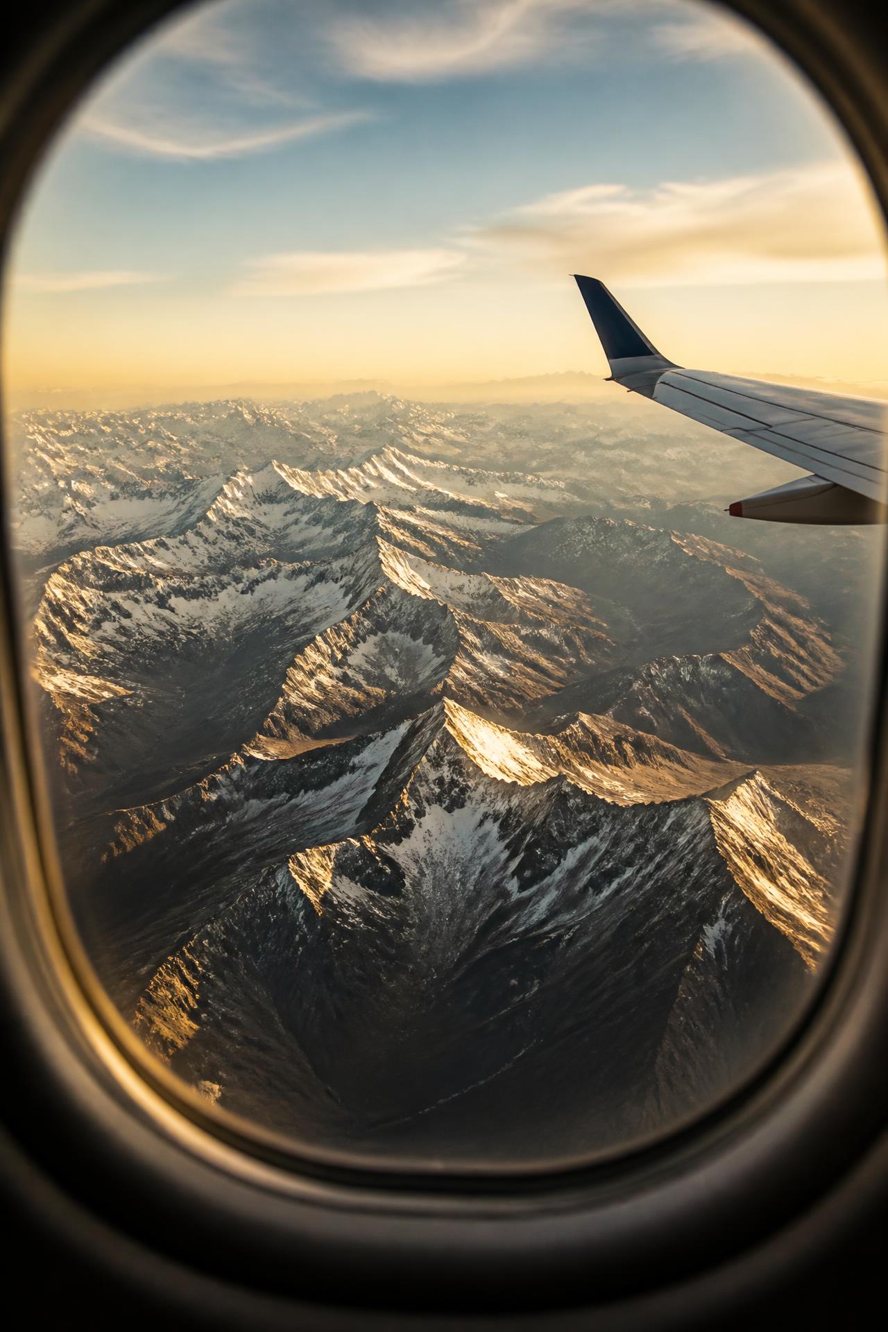 Vista aérea da Cordilheira dos Andes nevada pela janela de um avião, sob a luz da manhã